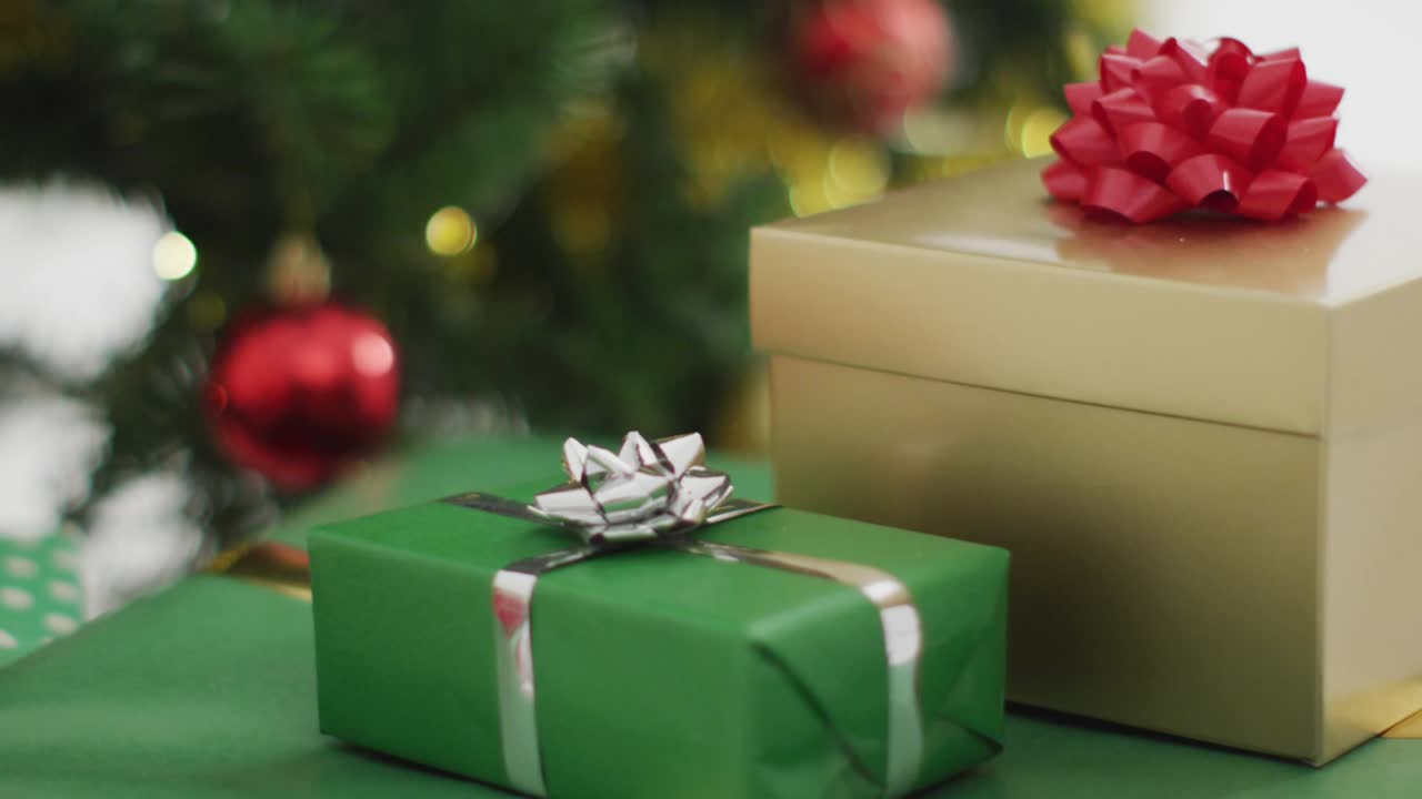 Snowflakes drifting, camera focusing from green gift box to swinging red ornament revealing tree