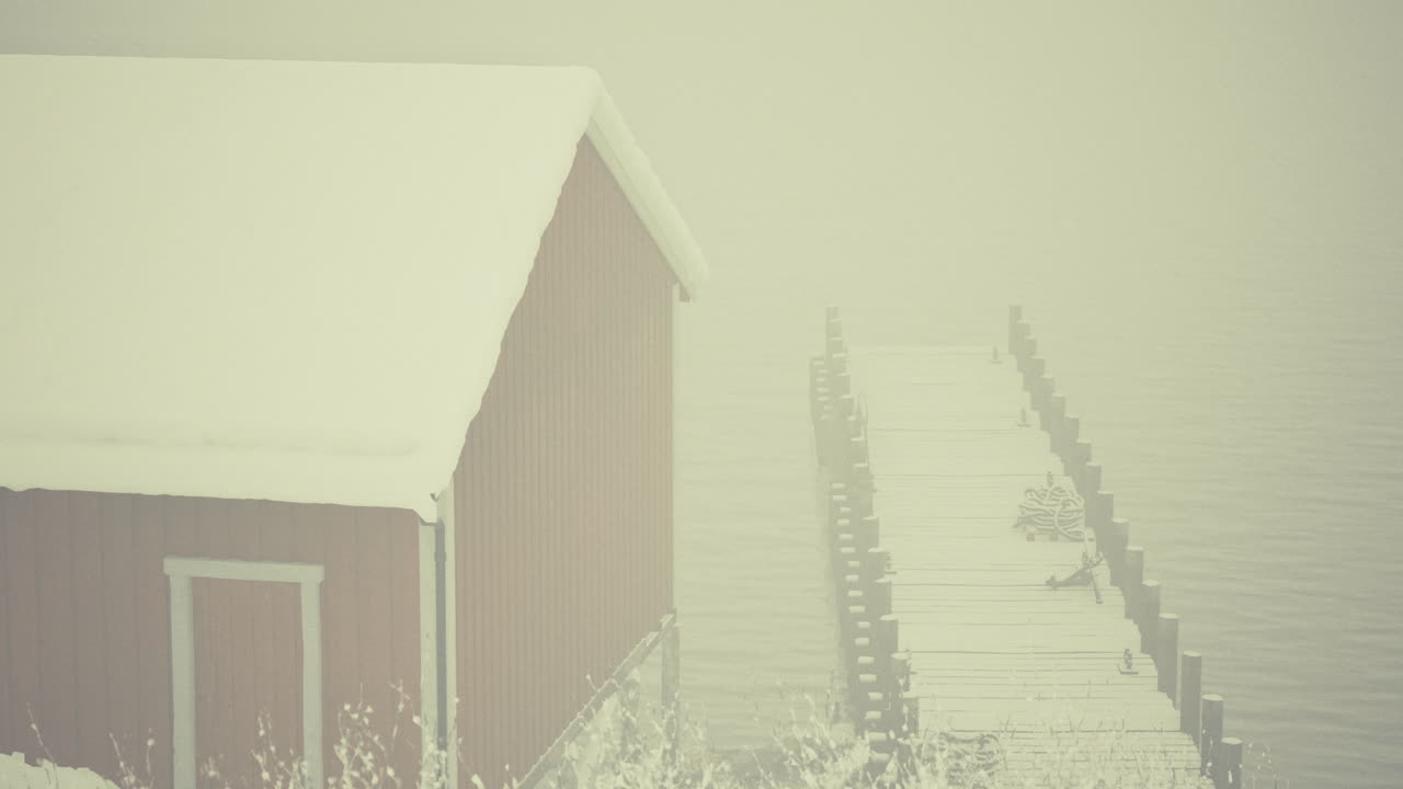 Snow covered cabin and dock on a misty winter day by the lake