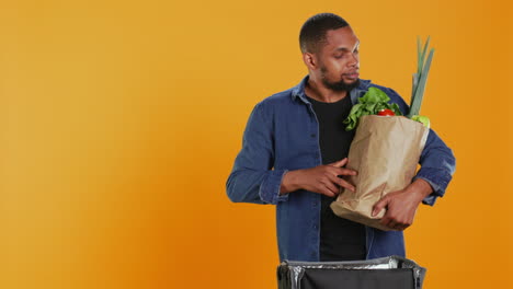 empleado de comida para llevar entregando una bolsa de papel llena de productos biológicos en una mochila térmica