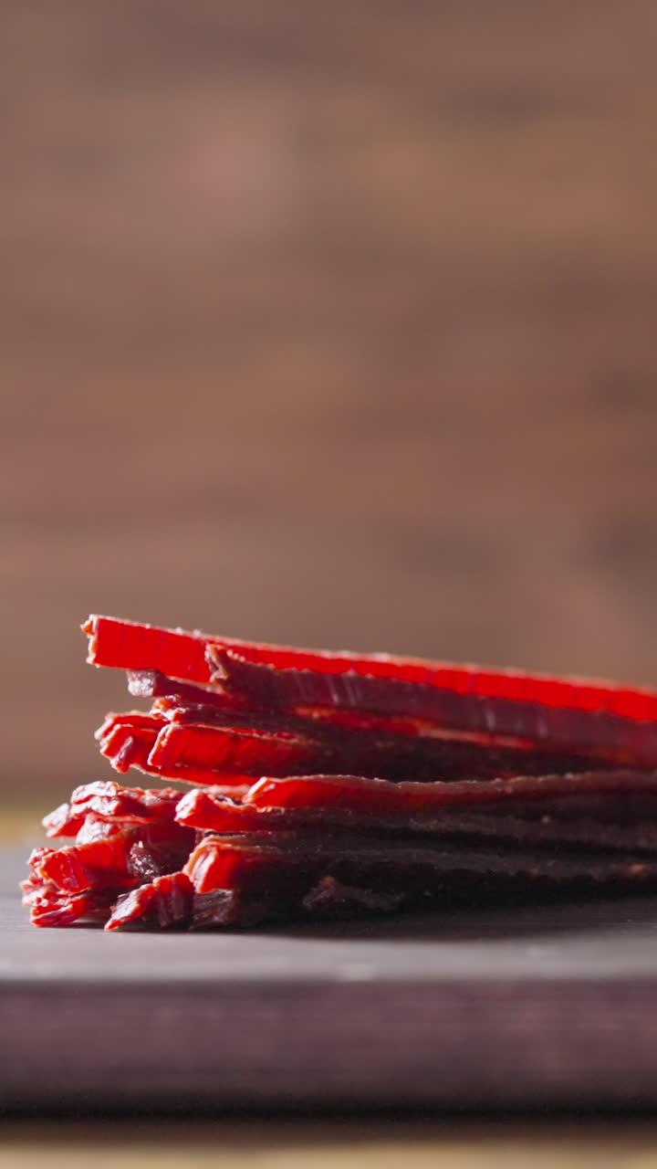 Heap of sun-dried salmon sticks and glass mug of fresh beer with rising up bubbles on rustic wooden cutting board in pub closeup slow motion