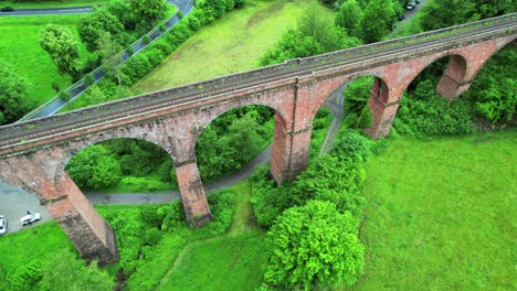 A-tall-brick-railway-bridge,-a-historic-viaduct-between-green-hills