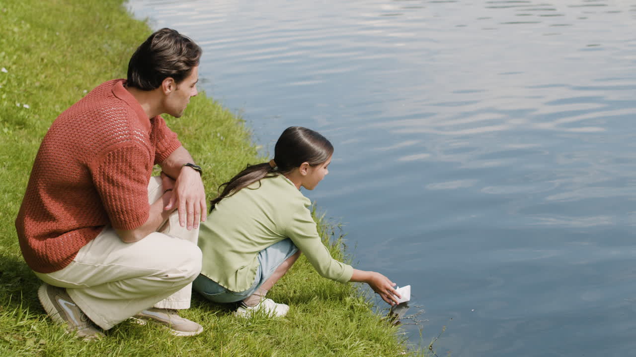 Father and daughter playing with a paper boat by the lake