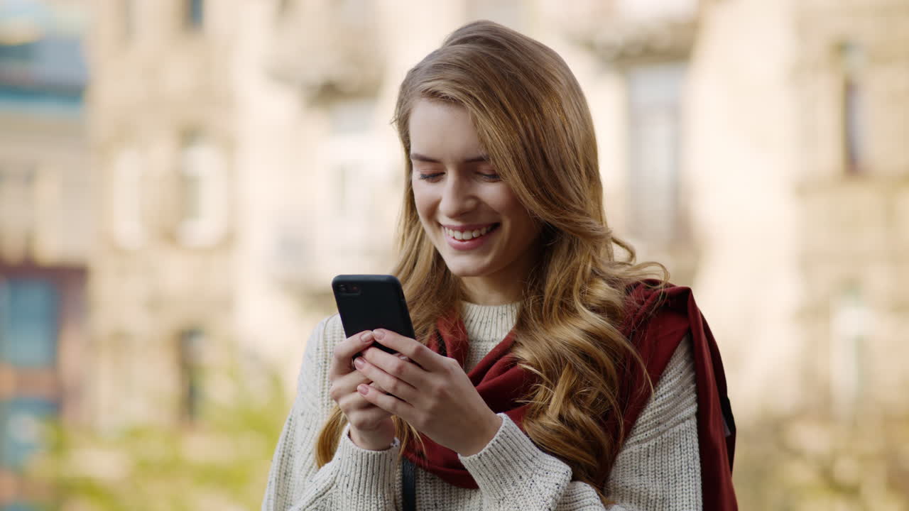 chica feliz enviando mensajes de texto al teléfono inteligente al aire libre. mujer alegre usando el teléfono en la calle.