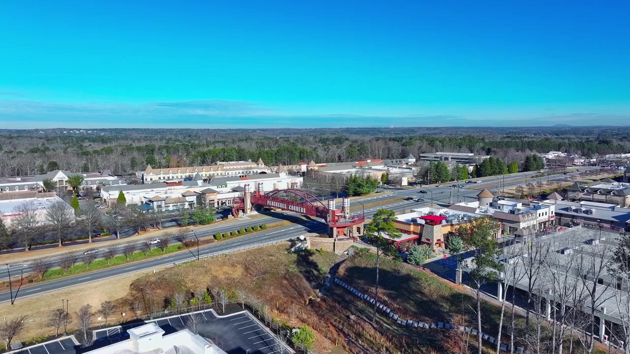 Vue par drone révélant le pont piétonnier de Peachtree Corners avec le centre commercial The Forum Peachtree Corners en arrière-plan, sur Peachtree Parkway (SR 141) en Géorgie.