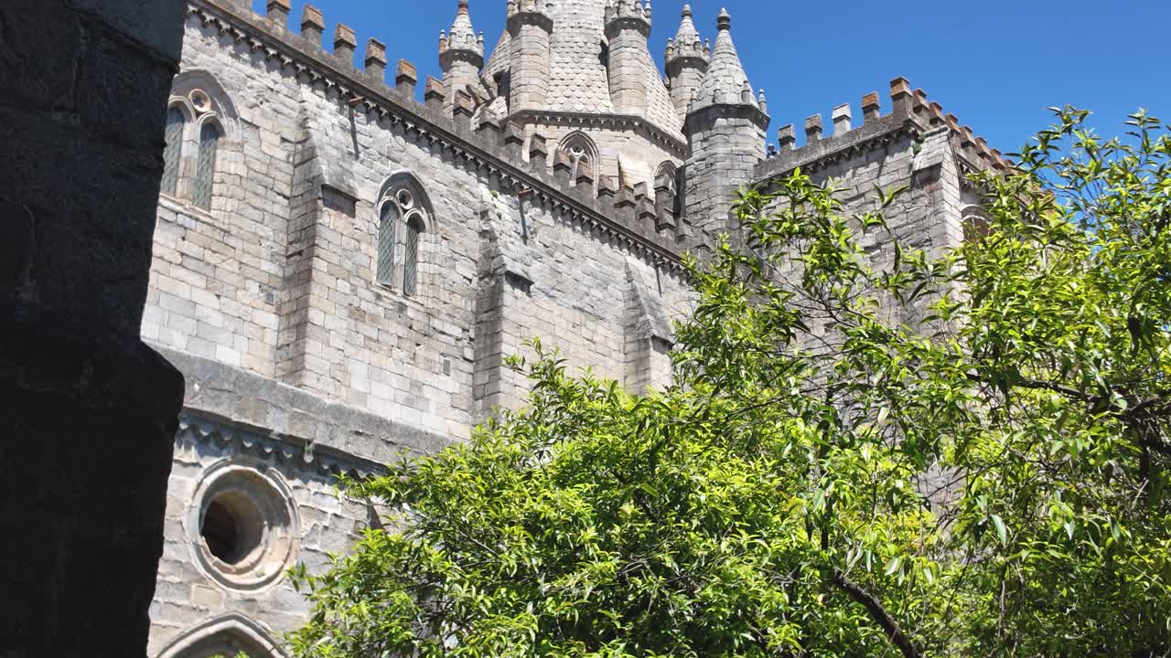 Stone cathedral towers above green cloister trees in Evora Portugal