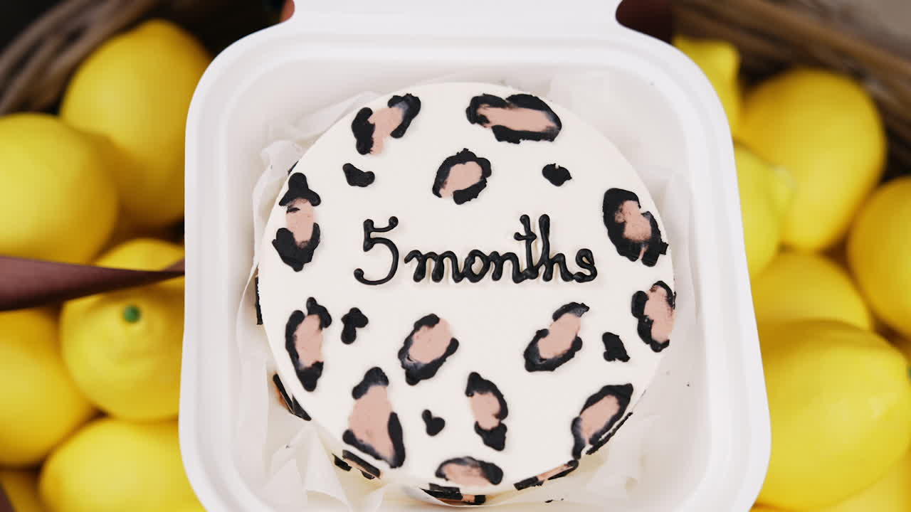 Male hand opening white plastic box with a cake inside. Five month anniversary celebration with a cake. Close up. Lemons at backdrop.