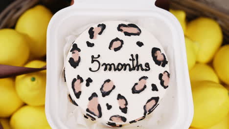 male hand opening white plastic box with a cake inside. five month anniversary celebration with a cake. close up. lemons at backdrop.
