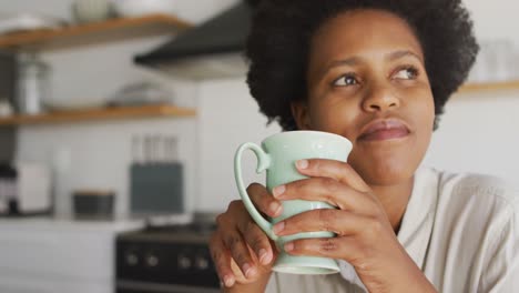 happy african american woman drinking coffee in kitchen