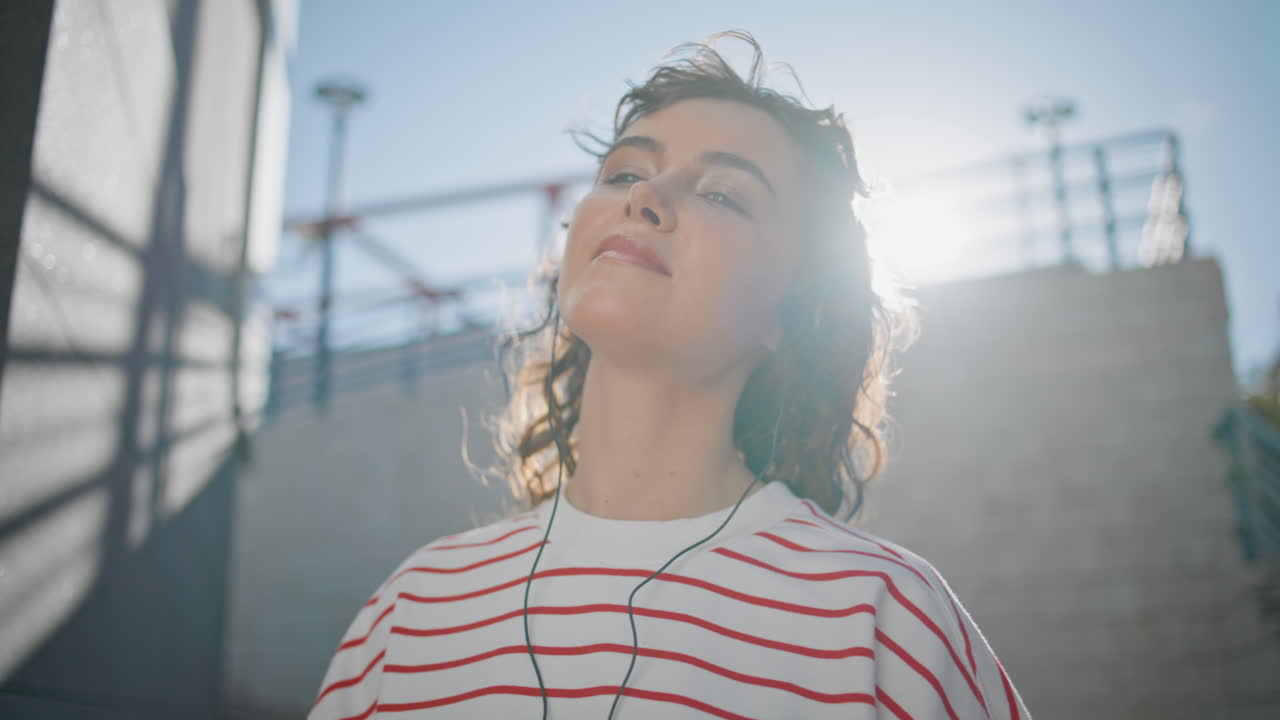 la chica de los auriculares relajándose la luz del sol moviéndose con tacto la canción al aire libre de cerca