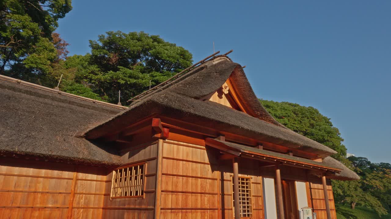A close-up of a charming traditional Japanese building, highlighting its intricate thatched roof and natural wooden walls against a clear sky.