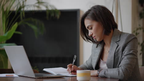 Empresaria-Analizando-El-Gráfico-Y-Escribiendo-En-La-Computadora-Portátil.-Trabajo-Remoto-Mujer-Joven-Con-Anteojos-Escribe-Notas-En-El-Portapapeles-Y-Escribe-En-El-Teclado-De-La-Computadora-Portátil