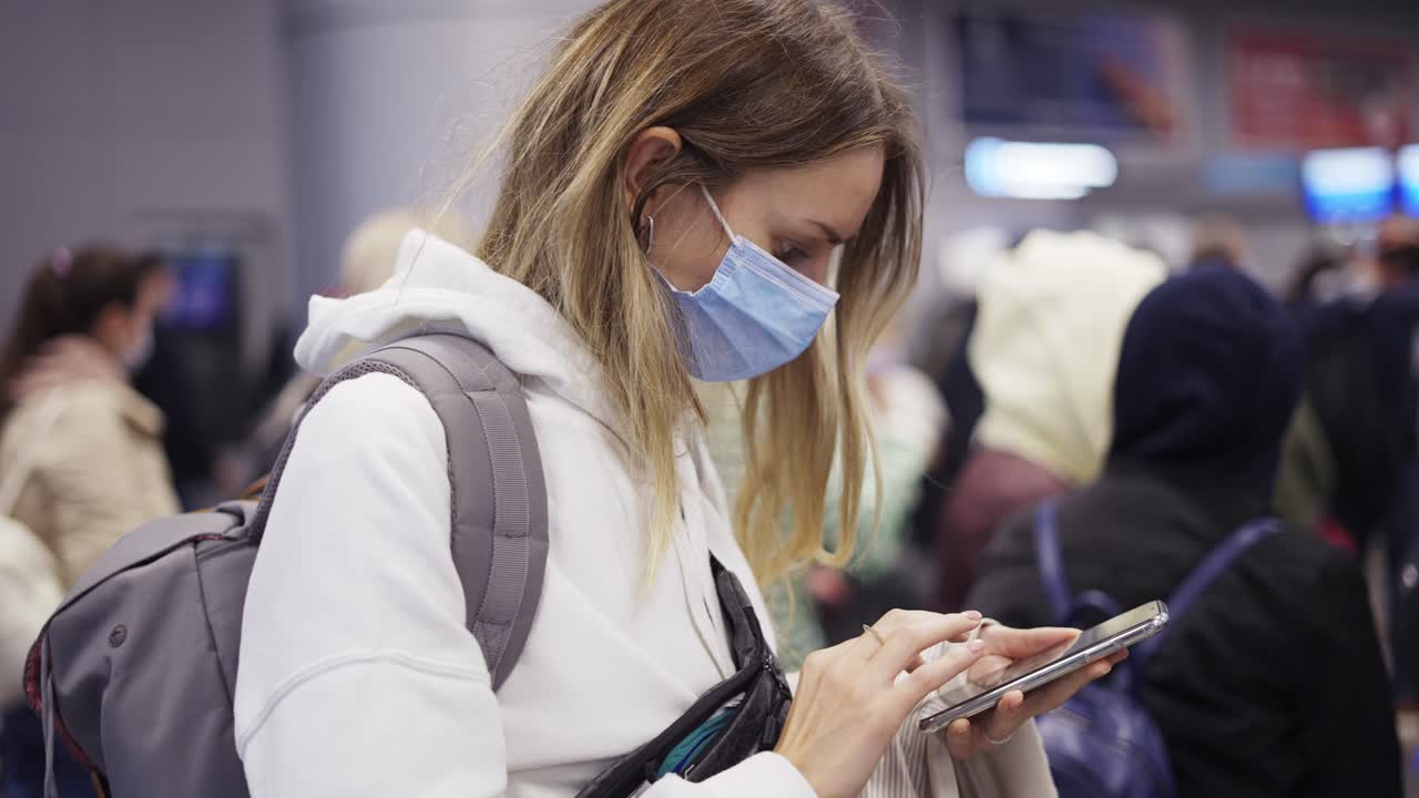 mujer con máscara usando teléfono celular personal mientras espera un vuelo en la multitud del aeropuerto