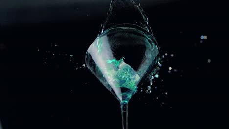 Ice-falling-into-cocktail-glass-of-blue-liquid-low-angle