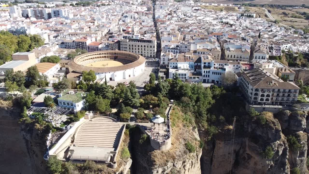 Aerial shot of circular Plaza de Toros bullring surrounded by white buildings and trees near steep cliffs, showcasing striking contrast between historic architecture and dramatic natural terrain.