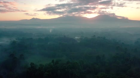 sliding drone shot of famous borobudur temple during sunrise in the morning in slightly foggy weather and cloudy sky - magelang,indonesia