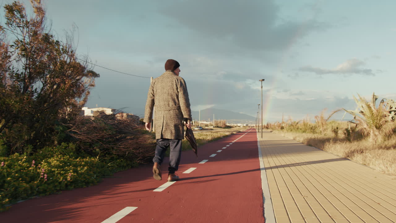 Elderly Man Walks on the Bike Lane Holding an Umbrella