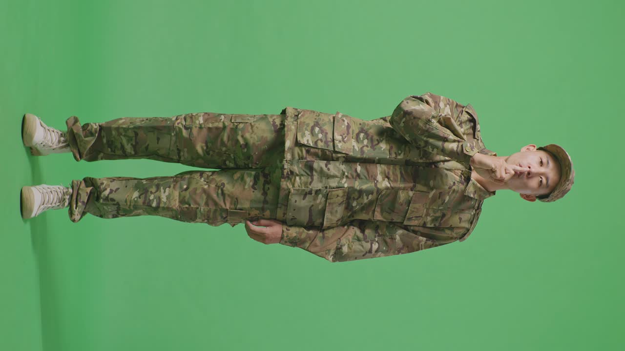 Full Body Of Asian Man Soldier Looking At Camera And Making Shh Gesture While Standing In The Green Screen Background Studio