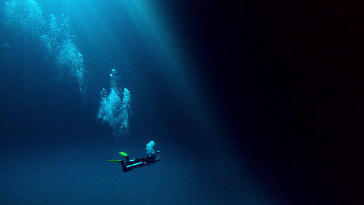 buzo en una enorme cueva submarina azul con el agujero del sol en la parte superior