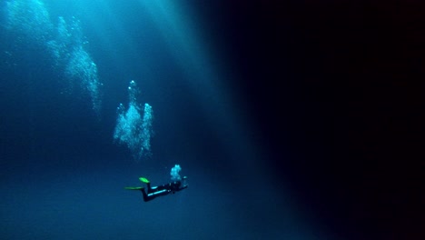 scuba diver in a huge blue underwater cave with the sun hole on top