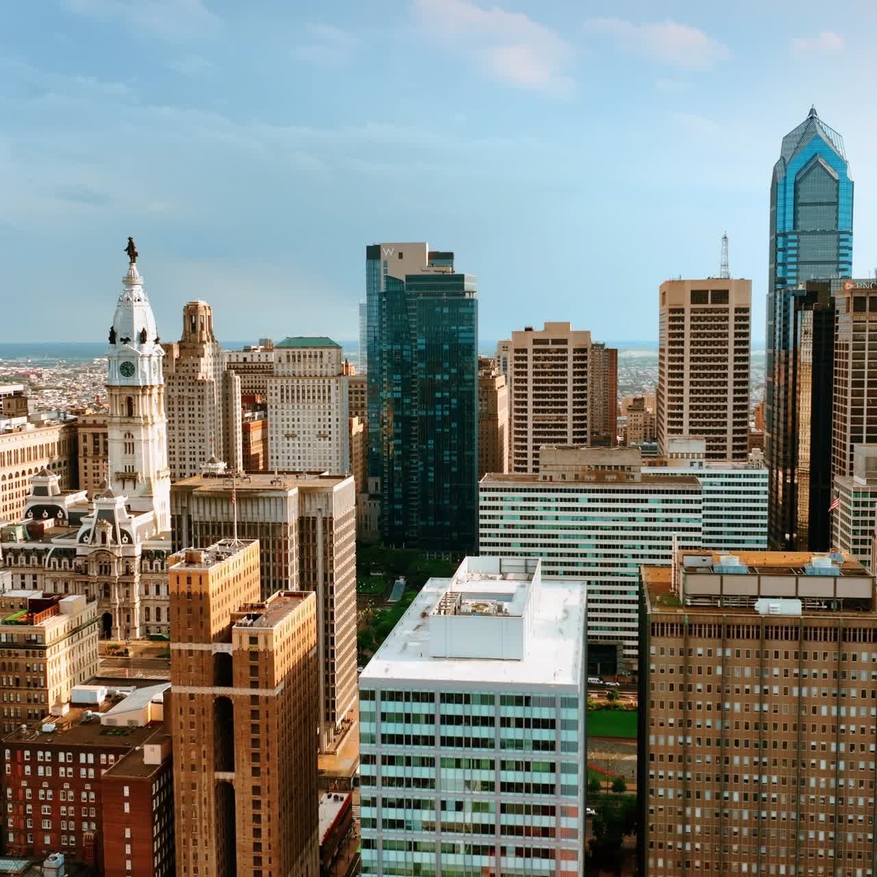 Tops of skyscrapers towering above multi-storied buildings. Drone footage slowly rising above Philadelphia cityscape