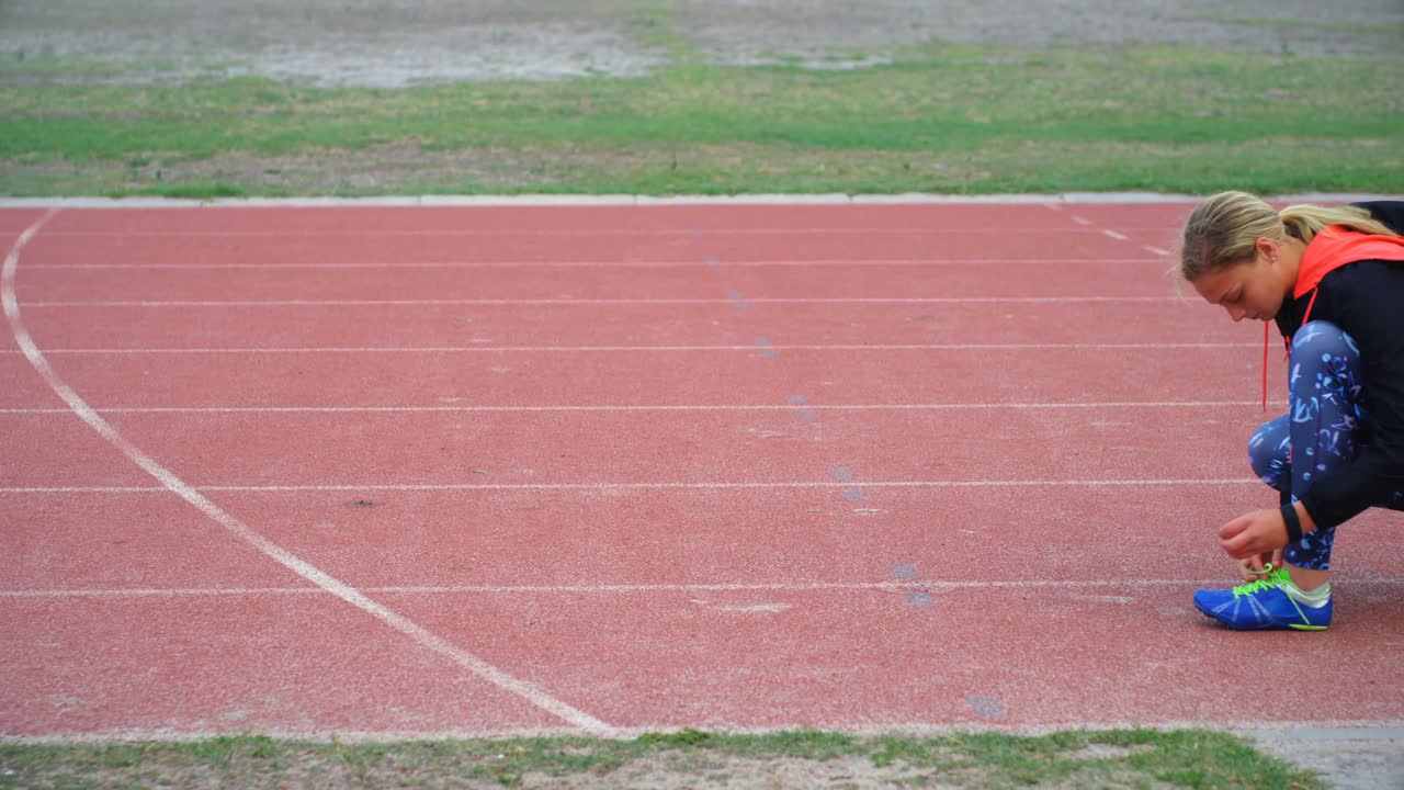 vista lateral de una joven atleta caucásica atando el cordón de los zapatos en la pista de carrera 4k