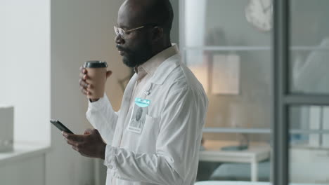 African-American-Doctor-Drinking-Coffee-and-Using-Phone-at-Work