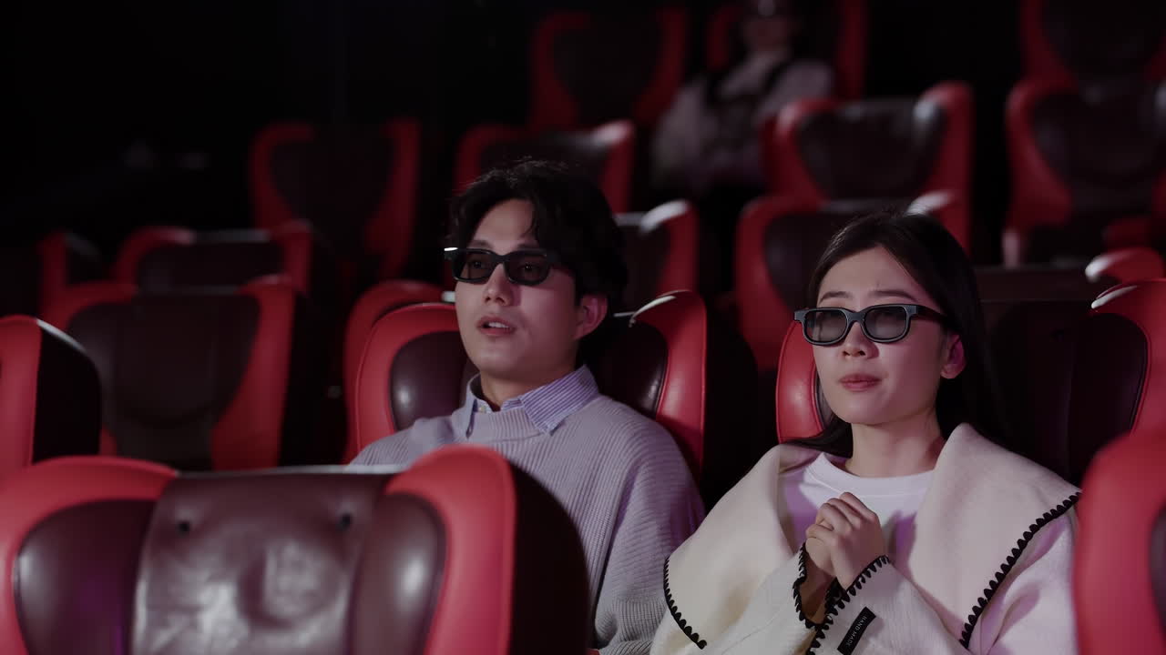 Giovane coppia sbalordita che guarda un'esperienza cinematografica 3D indossando occhiali 3D su comode poltrone in un auditorium cinematografico. Esperienza cinematografica, intrattenimento, relax, evasione