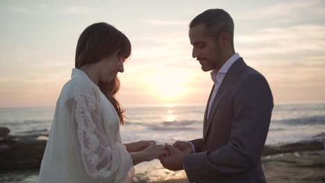 groom putting ring on finger of bride on sea shore