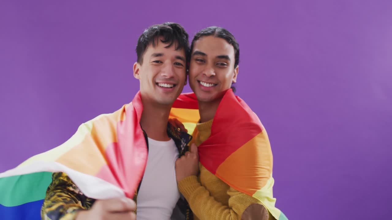Portrait of happy diverse male couple holding lgbt flag and embracing