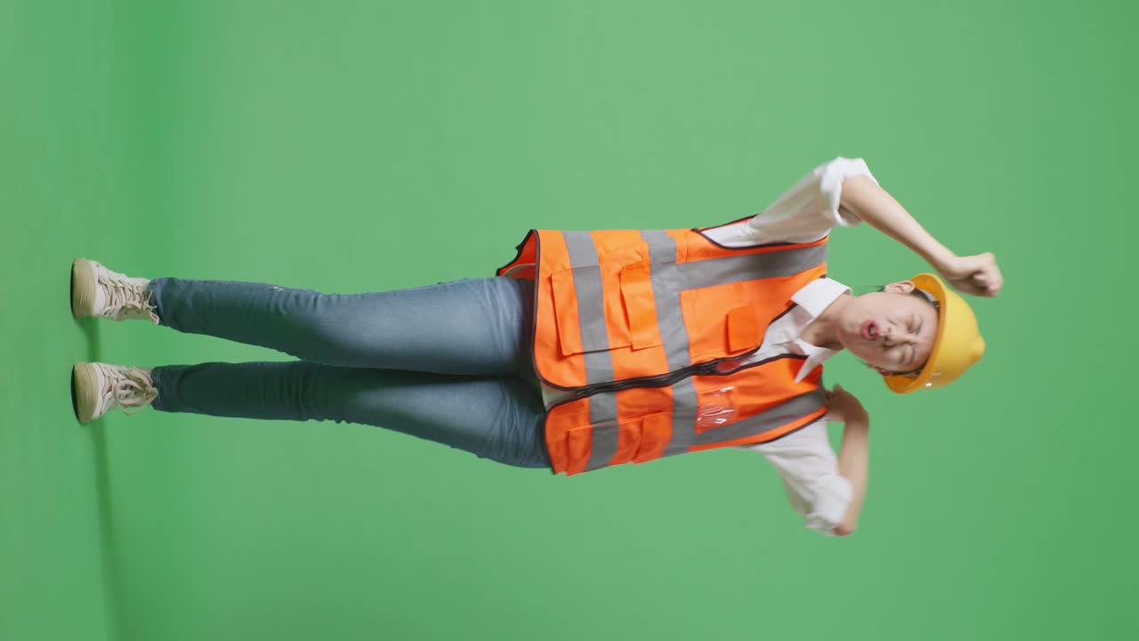 안전 헬을 입은 아시아 여성 엔지니어의 몸이 가득 차 있고, 골을 비명을 지르고, 녹색 스크린 배경 스튜디오에서 춤을 추며 축하하고 있습니다.