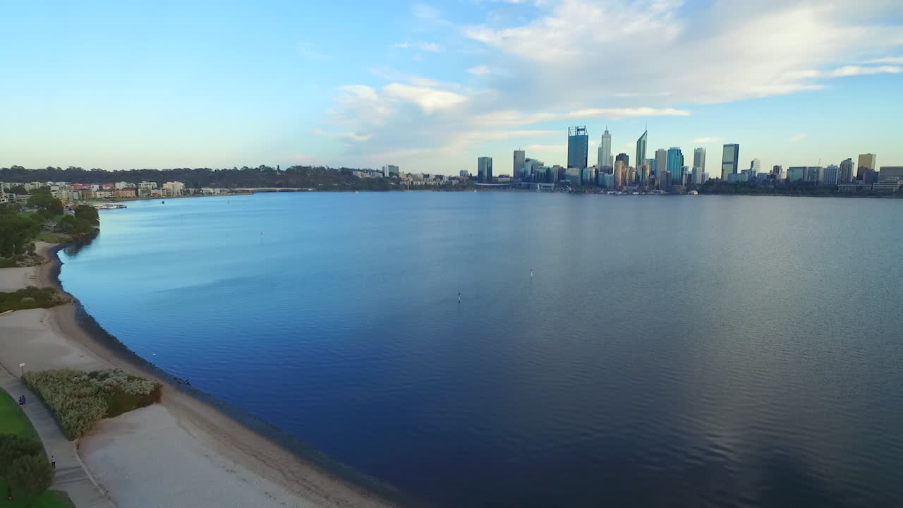 Drone flys up and over Australian flag pole in park, Perth city and swan river in background