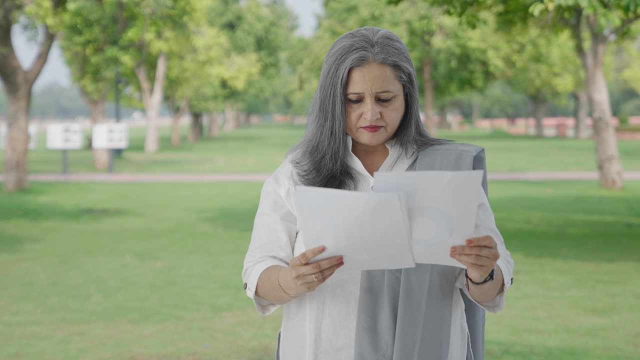 Mujer india mayor leyendo informes en el parque