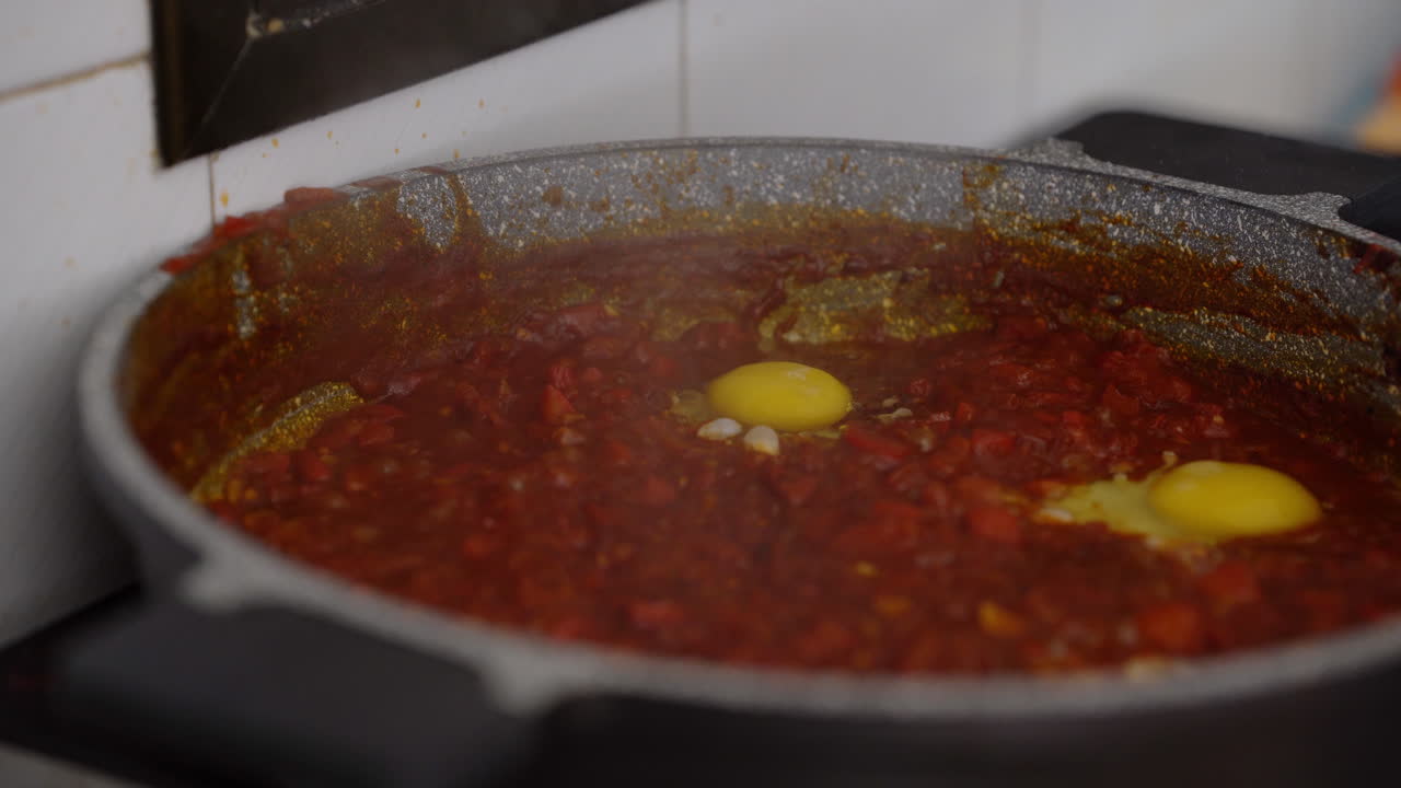 el hombre rompe un huevo en una salsa de tomate burbujeante, preparación de shakshouka casero, filmado con luz natural