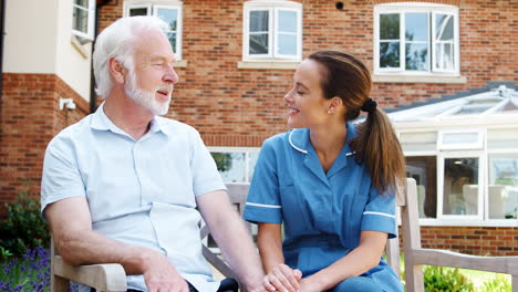 Senior-Man-Sitting-On-Bench-And-Talking-With-Nurse-In-Retirement-Home