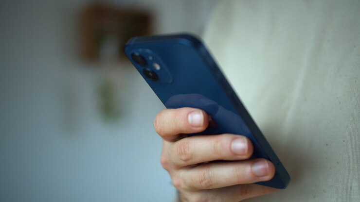 Vista posteriore di uno smartphone, un uomo che tiene in mano uno smartphone blu e ci chatta, in piedi su sfondo bianco