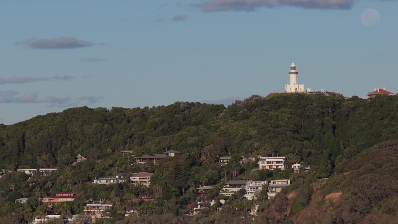 Faro de Cape Byron sobre el barrio frente a la playa de Wategos en Byron Bay, Nueva Gales del Sur, Australia. Toma aérea con inclinación ascendente