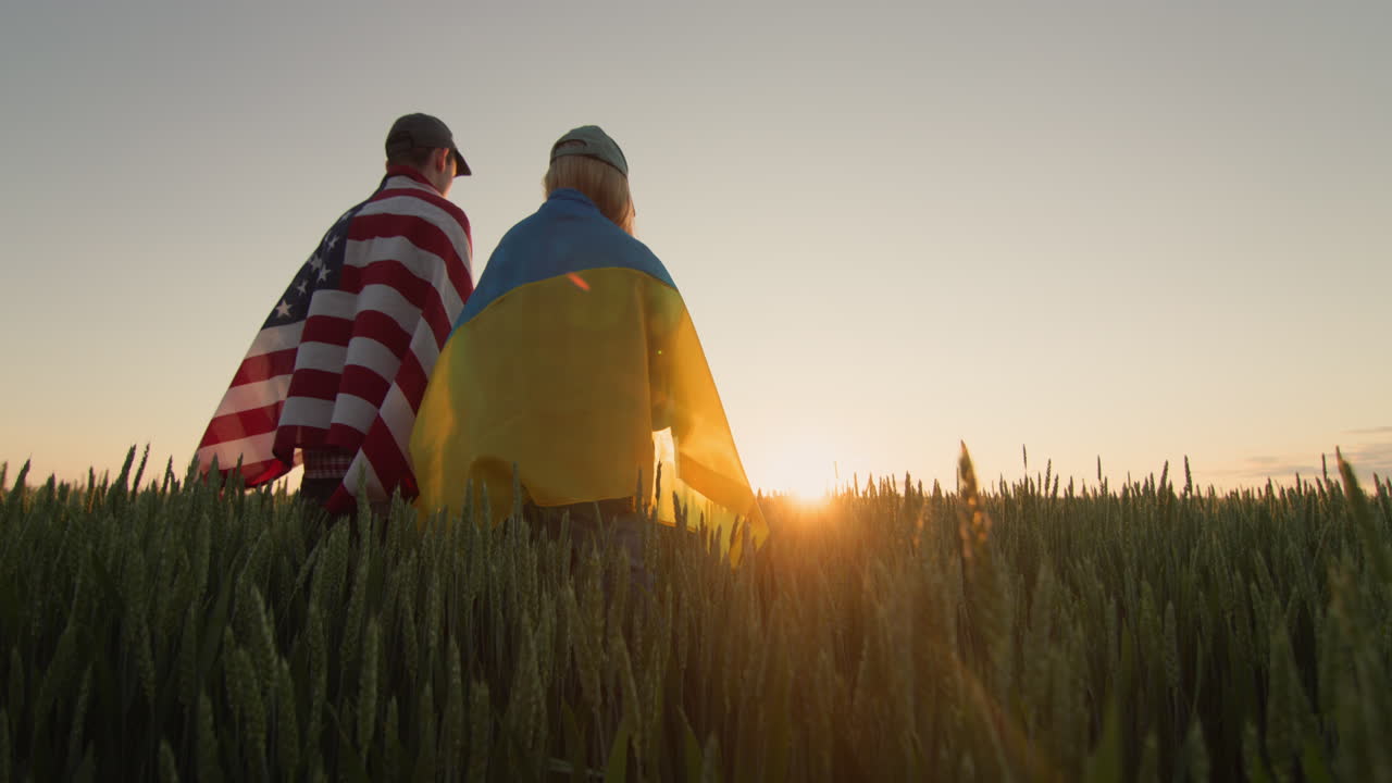 una pareja joven con banderas de estados unidos y ucrania en un campo de trigo.