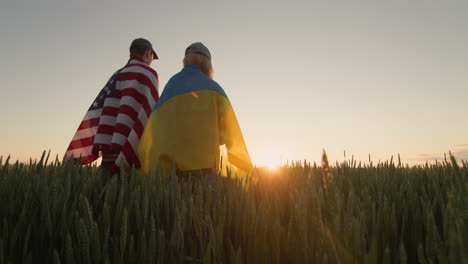 young couple with usa and ukraine flags in wheat field. low angle view