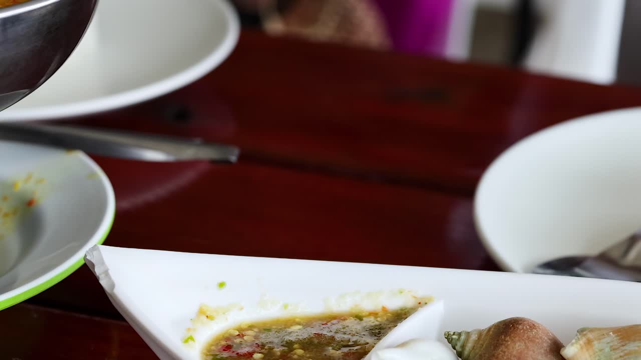 Close-up of hands dipping seafood into a spicy sauce on a wooden table.