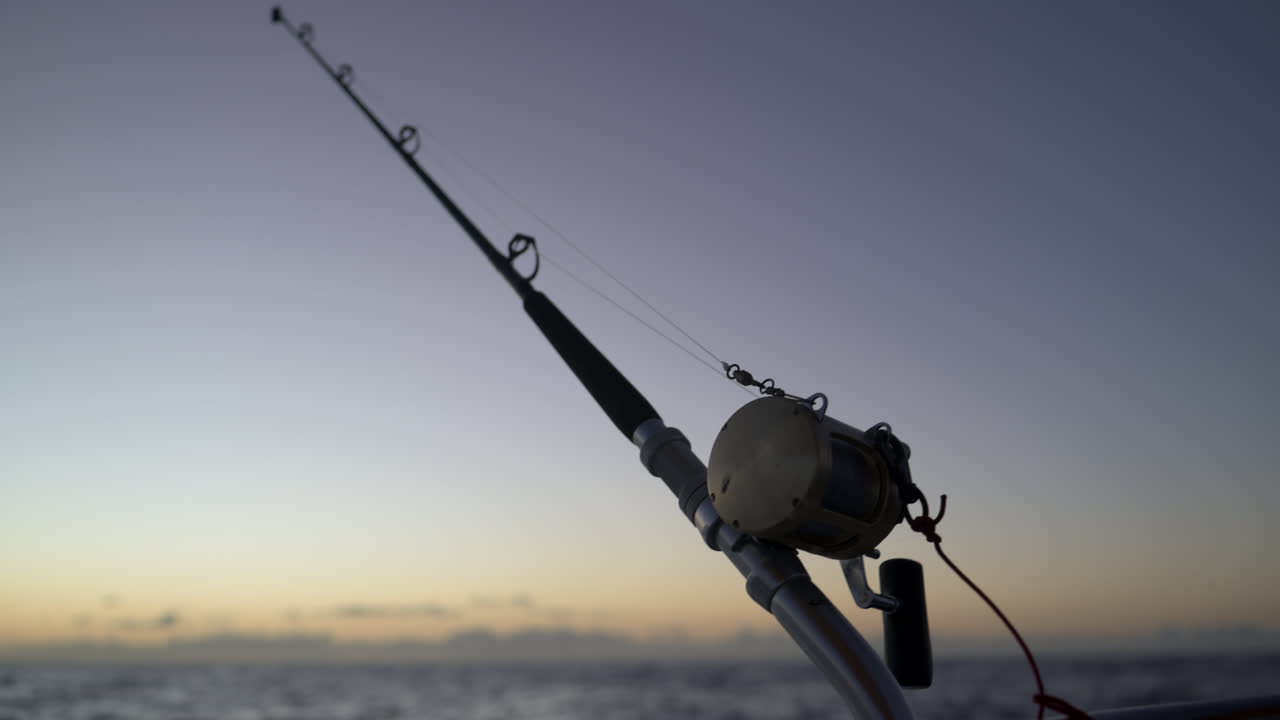Ripresa al rallentatore di una canna da pesca sullo sfondo di un sole che sorge sull'Oceano Pacifico