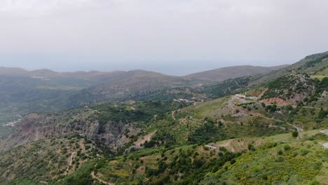 Aerial-showing-beautiful-green-mountains-with-curved-roads-under-a-cloudy-sky