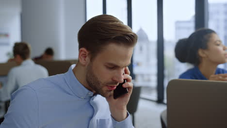 Businessman-talking-on-mobile-phone-at-workplace.-Team-working-in-open-space