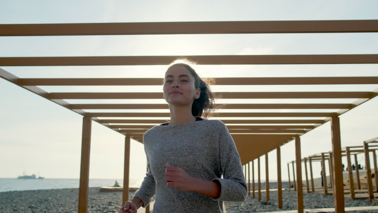 mujer corriendo en una playa con una pérgola de madera
