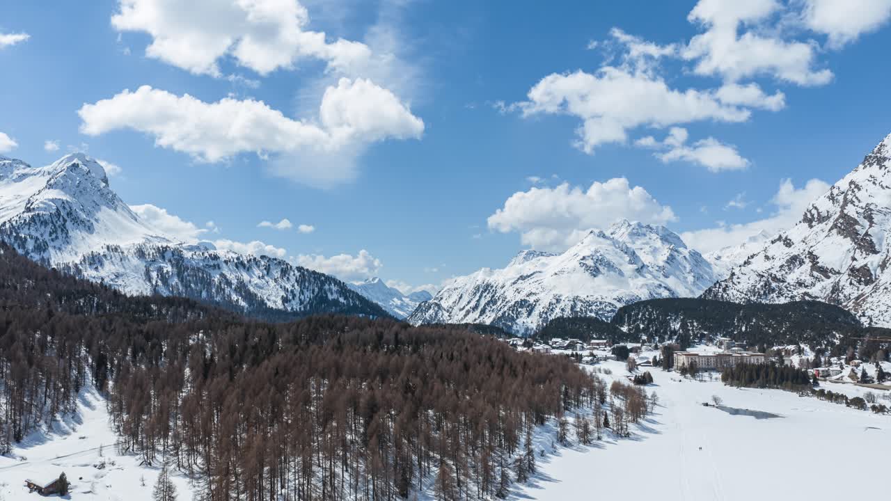 Lembah Maloja Alpen Swiss menampilkan gunung-gunung bersalju, hutan pinus, dan langit biru. Hyperlapse udara.