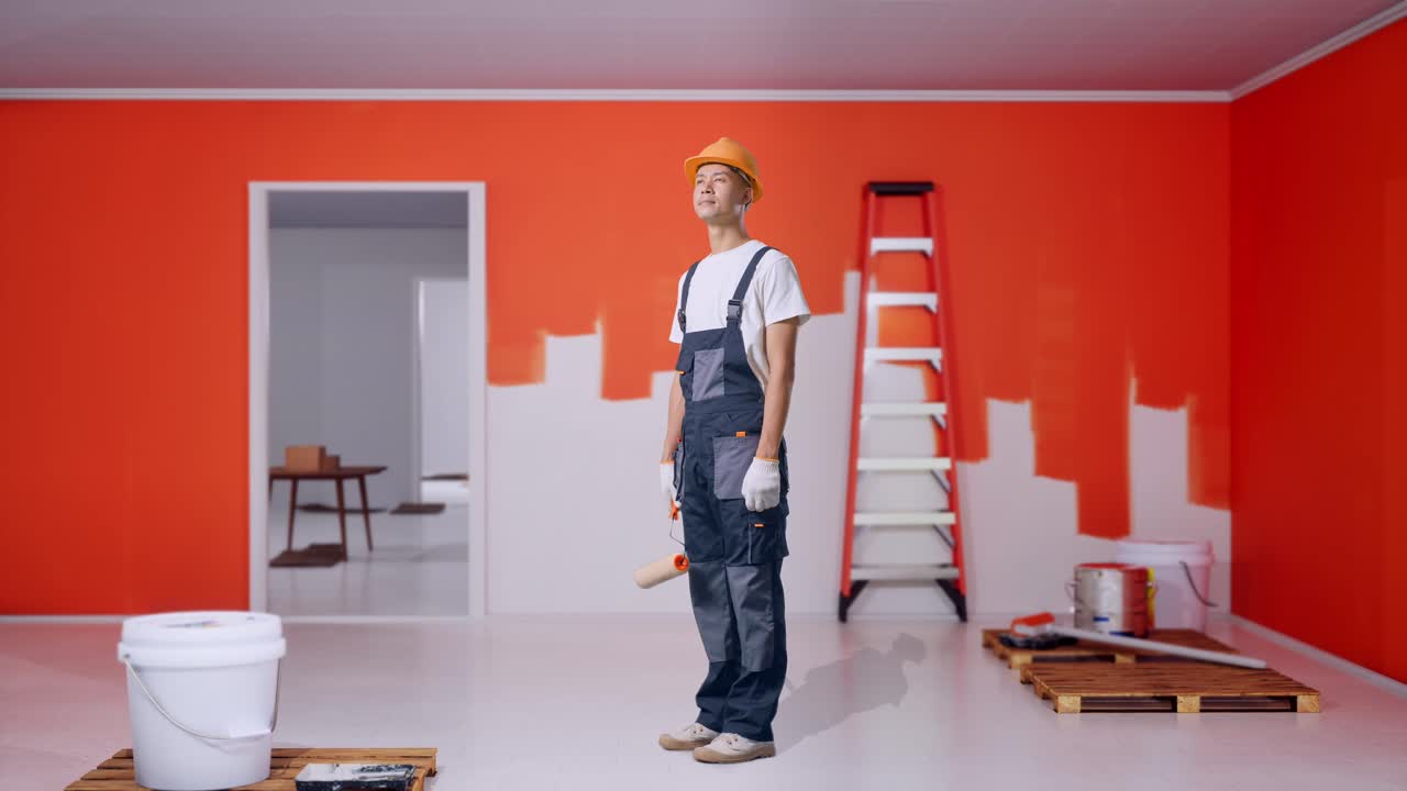 Full Body Of Side View Asian Man Painter Wearing Safety Helmet Standing And Look Around With Painting Wall In Room