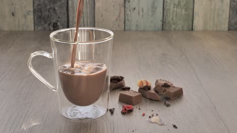 glass filled with chocolate milk on wooden table with chocolate pieces