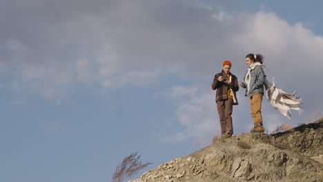 dos adolescentes vestidos de invierno hablando en la cima de una montaña en un día ventoso