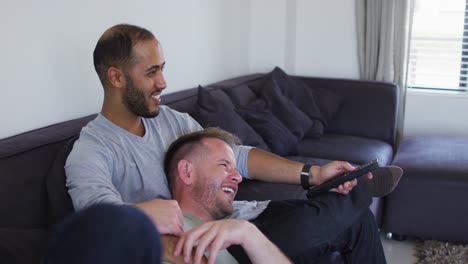 Multi-ethnic-gay-male-couple-sitting-on-couch-and-watching-tv