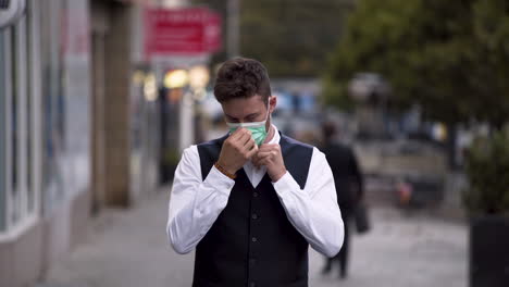 an elegant young man wearing a black waistcoat and white shirt putting on a green protective covid-19 mask, trying it and then throwing it away contemptuously over his shoulder and smiling, 4k