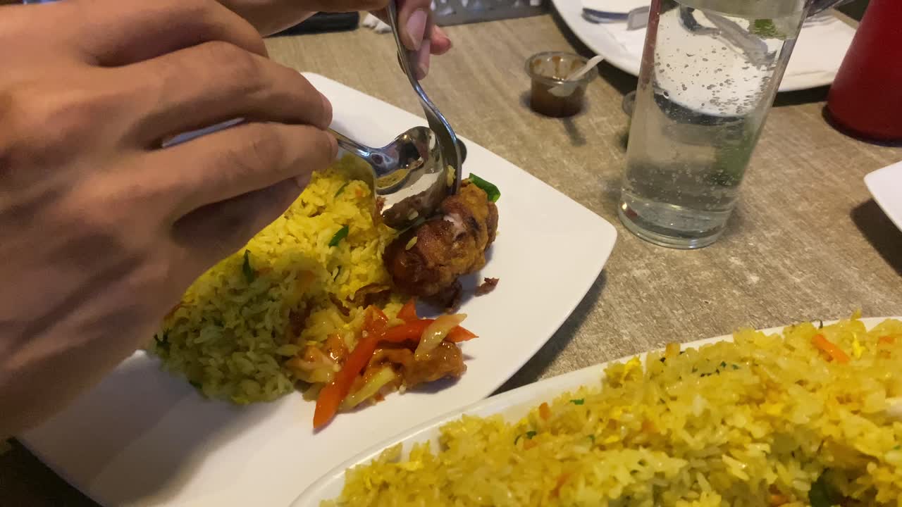 separando suavemente el trozo de pollo frito con cubiertos en el plato junto al arroz frito en el restaurante